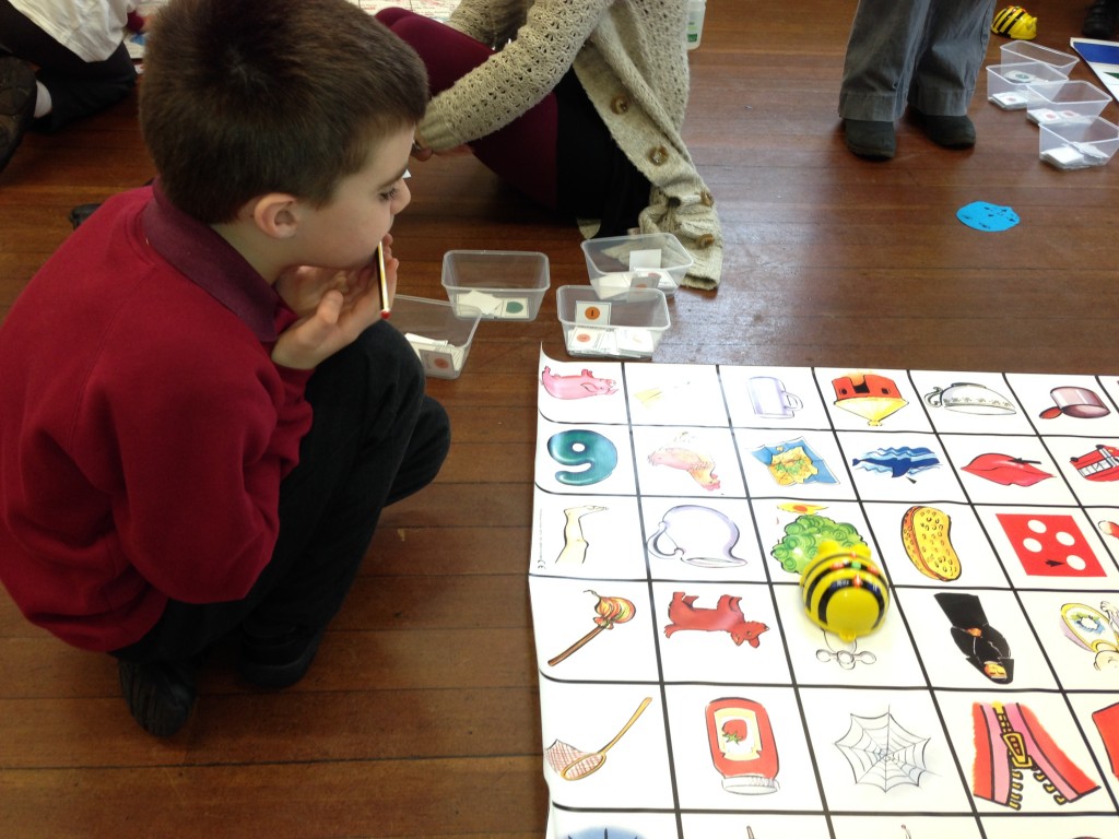 A photo of a young child considering a Bee-Bot on a floormat.