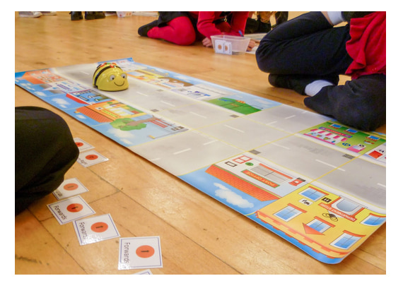 Children working with a Bee-Bot moving around a floormat of a street.